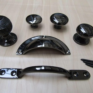 May include: A set of five black cabinet knobs and pulls. The set includes two round knobs, one with a ribbed design, one curved pull, and two smaller round knobs. The hardware is made of metal and has a black finish.