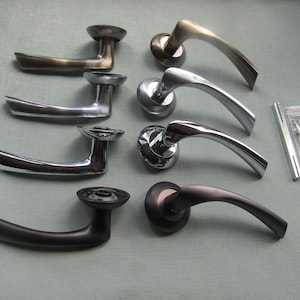 May include: Six different door handles in various finishes, including brass, chrome, and black. The handles are all in the same style, with a curved lever and a round base.