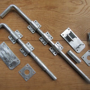 May include: Two silver metal door bolt locks with a square strike plate, a round strike plate, and a bag of screws.