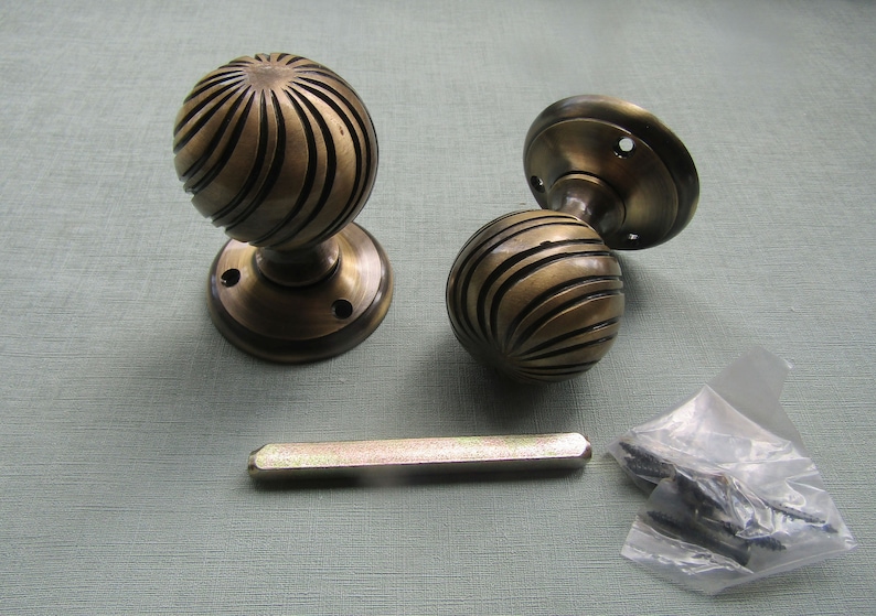 May include: Two antique brass door knobs with a spiral design. The knobs are attached to round plates. A metal rod and a bag of screws are also included.