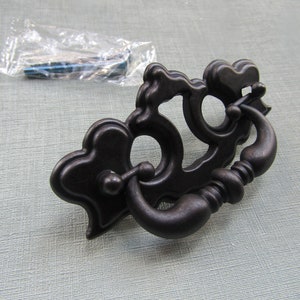 Peut inclure: Une poignée de tiroir en métal noir avec un design orné et une poignée incurvée. La poignée mesure environ 7,5 cm de long et 3,8 cm de large.