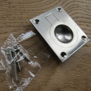 May include: A brushed nickel flush pull handle with a round recessed opening. The handle comes with four screws in a clear plastic bag.