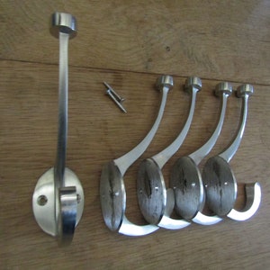May include: Five silver metal hooks with a curved design and a round base. The hooks are arranged in a row, with the base of each hook facing the viewer. The hooks are designed to be mounted on a wall.