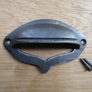 May include: A black cast iron drawer pull with a curved top and a rounded rectangular opening. The pull is designed to be used with two screws.
