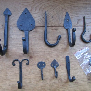 May include: A set of ten black metal hooks with various designs, including leaf, heart, and scroll shapes. The hooks are displayed on a wooden surface and come with screws for installation.