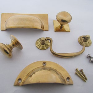 Könnte beinhalten: Ein Satz aus sechs Messing-Schrankbeschlägen, darunter zwei Schubladenzüge, zwei Knöpfe, ein Griff und ein kleiner Knopf mit quadratischer Basis. Die Beschläge sind poliert und haben eine glänzende Oberfläche.