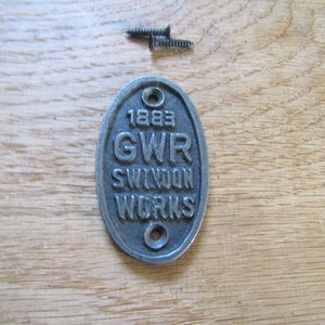 May include: A silver oval-shaped metal plaque with the text "1883 GWR SWINDON WORKS" on it.