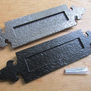 May include: Two metal mail slots with a decorative fleur-de-lis design. One is black and the other is gray.