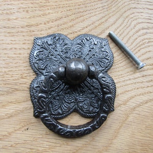 May include: Black cast iron drawer pull with a decorative floral design and a ring handle. The pull comes with a screw for installation.