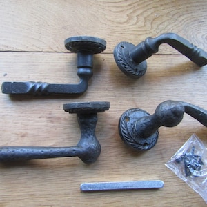 May include: Four black cast iron door handles with a decorative design. The handles are shown on a wooden surface with screws and a metal plate.