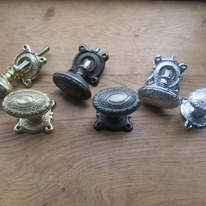 May include: Four antique door knobs in different finishes: brass, black, and chrome. Each knob features an oval design with intricate details.