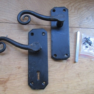 May include: Two black door handles with a decorative scroll design on the lever. The handles are shown with their backplates and mounting hardware.