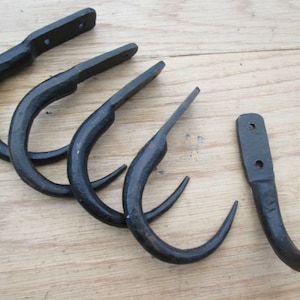 May include: Six black metal hooks with a curved design. The hooks are made of wrought iron and have a rustic finish.