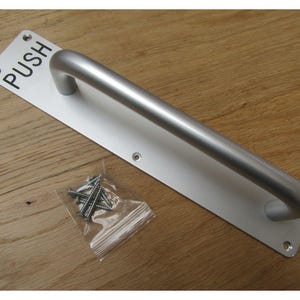 May include: A silver door handle with a push sign. The handle is a curved bar with a rounded end. The sign is printed in black on a rectangular plate.
