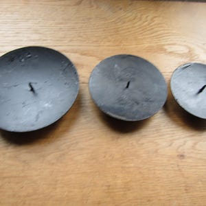 May include: Three black metal candle holders of different sizes. The holders are round and have a small hole in the centre for a candle.