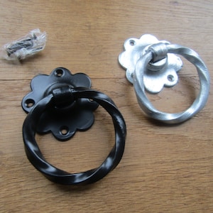 May include: Two twisted ring door handles with a decorative flower-shaped base. One handle is black and the other is silver.