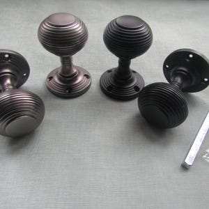 Könnte beinhalten: Vier dekorative Türknöpfe mit geripptem, kugelförmigem Design. Zwei sind dunkelgrau, zwei sind schwarz. Jeder Knopf hat eine kreisförmige Basis. Ein kleines Paket mit Schrauben und ein Metallwerkzeug sind ebenfalls enthalten.