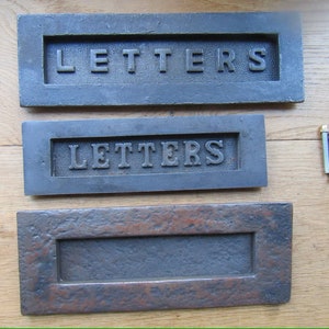 May include: Three rectangular metal letter plates in shades of grey and brown. The word "LETTERS" is embossed on the top two plates. Two screws are visible. These plates are likely for a mailbox or door.
