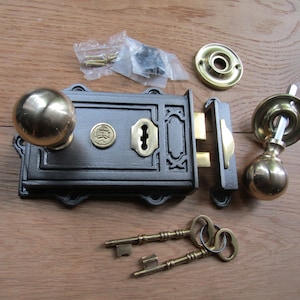 May include: A black cast iron door lock with brass accents and two keys. The lock has a decorative design and a round knob. The set includes a matching door handle with a round knob.
