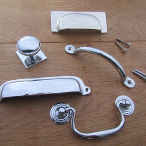May include: A set of five polished chrome cabinet hardware pieces, including two different styles of pulls, a knob, and two cup pulls. The hardware is arranged on a wooden surface.