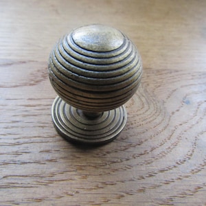 Könnte beinhalten: Ein Vintage-Schrankknauf aus Messing mit kugelförmigem Design. Der Knauf hat konzentrische Rillen und eine kreisförmige Basis. Das Messing hat eine warme, gealterte Patina, auf einer Holzoberfläche.