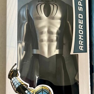 Pu&ograve; includere: Action figure di Spider-Man corazzato in una confezione di plastica trasparente. La figura &egrave; argentata e nera con un'emblema di ragno sul petto. La confezione include il testo "ARMORED SPIDER-MAN" e "AGES 4+".