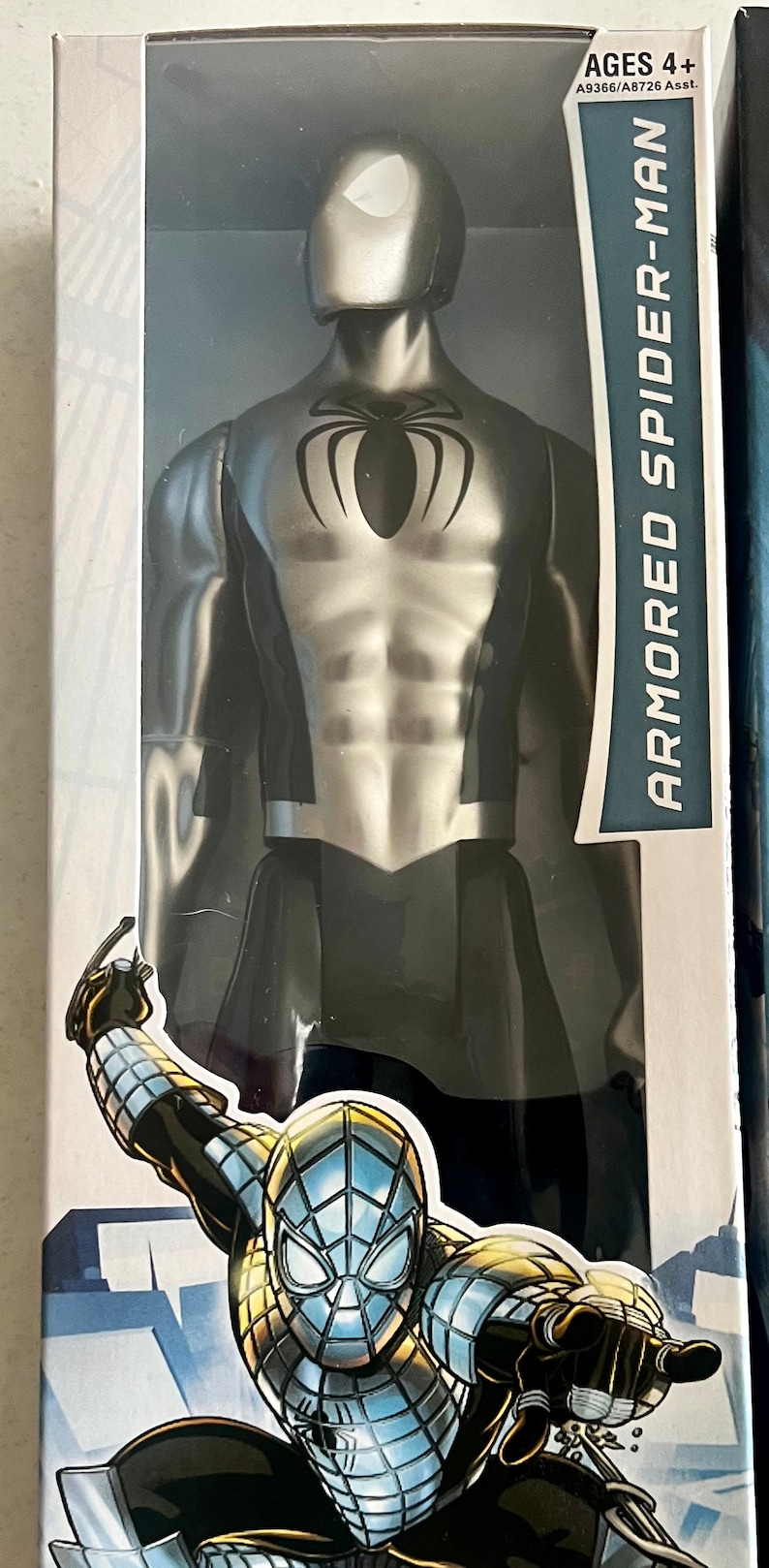 Pu&ograve; includere: Action figure di Spider-Man corazzato in una confezione di plastica trasparente. La figura &egrave; argentata e nera con un'emblema di ragno sul petto. La confezione include il testo "ARMORED SPIDER-MAN" e "AGES 4+".