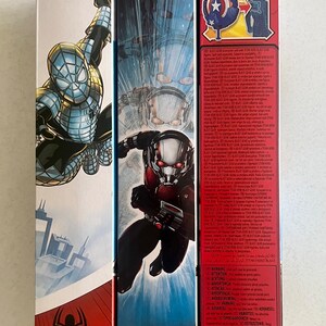 Pu&ograve; includere: Tre scatole di giocattoli della serie Titan Hero con personaggi Marvel. Le scatole mostrano Spider-Man, Ant-Man e Capitan America. Le scatole sono rosse, nere e bianche con illustrazioni dei personaggi e il logo "Titan Hero Series".