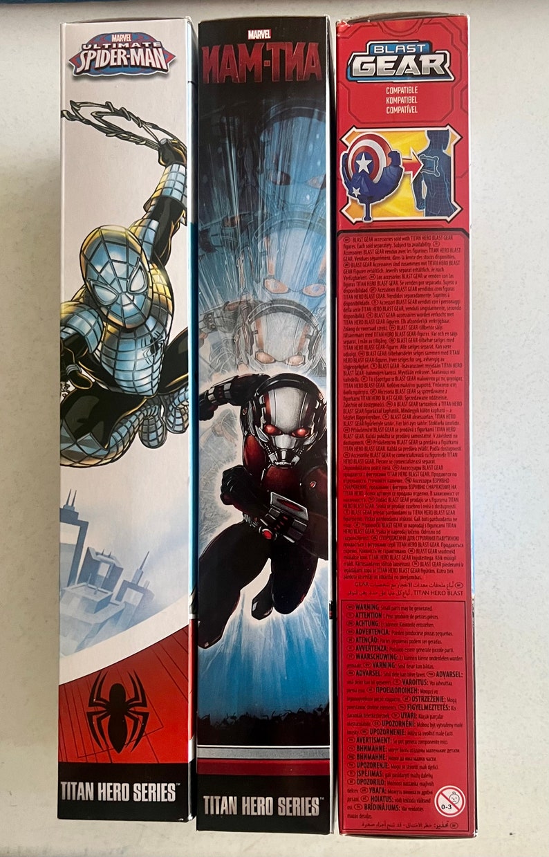 Pu&ograve; includere: Tre scatole di giocattoli della serie Titan Hero con personaggi Marvel. Le scatole mostrano Spider-Man, Ant-Man e Capitan America. Le scatole sono rosse, nere e bianche con illustrazioni dei personaggi e il logo "Titan Hero Series".