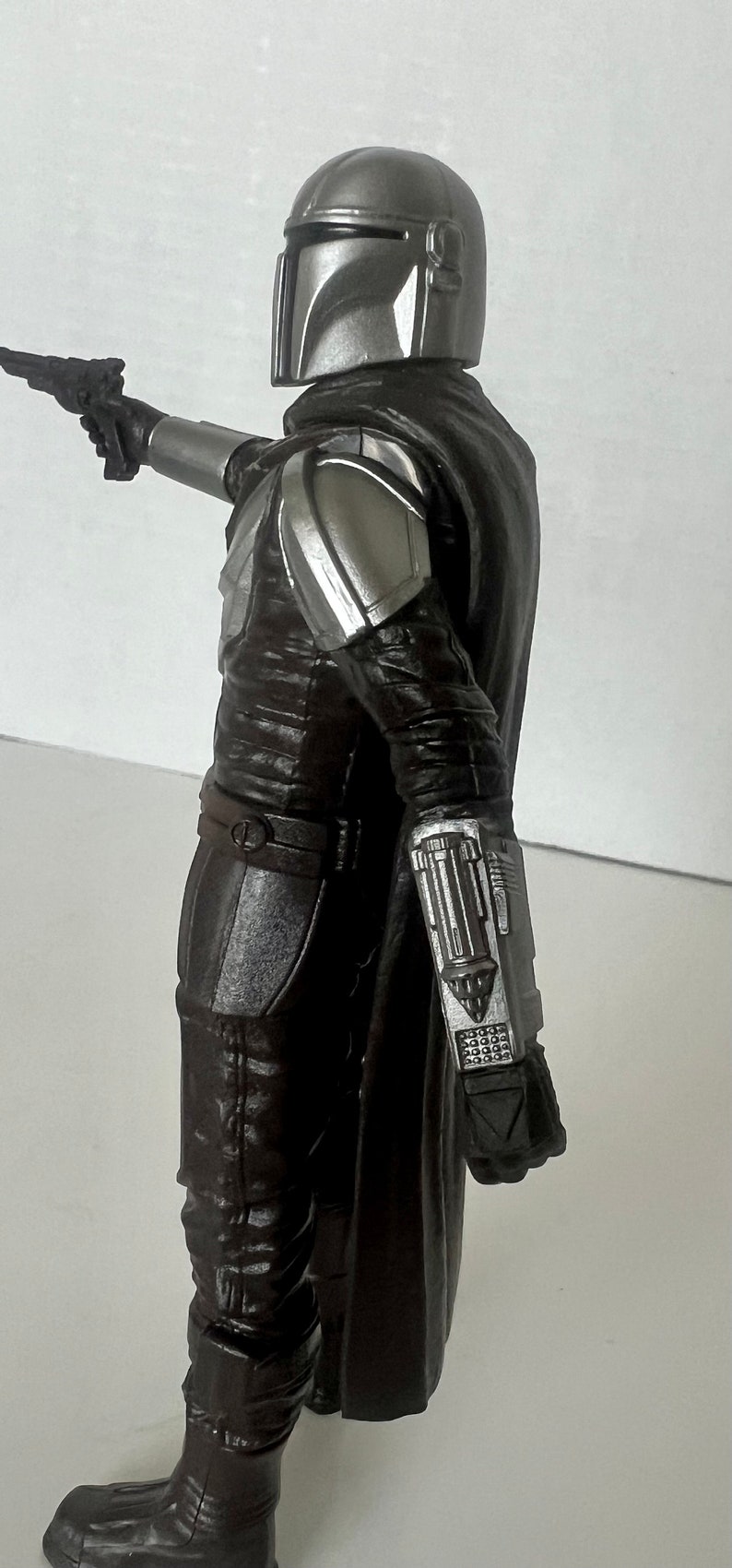 Puede incluir: Figura de acci&oacute;n detallada de un personaje de una serie de ciencia ficci&oacute;n. La figura viste una armadura marr&oacute;n oscuro con detalles plateados, un casco y una capa negra. Sostiene una pistola bl&aacute;ster.