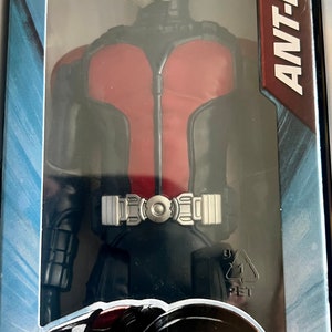 Pu&ograve; includere: Action figure di Ant-Man in una confezione di plastica trasparente. La figura indossa un costume rosso e nero con una cintura argentata. La confezione include il testo "ANT-MAN" e "EDAD 4+".
