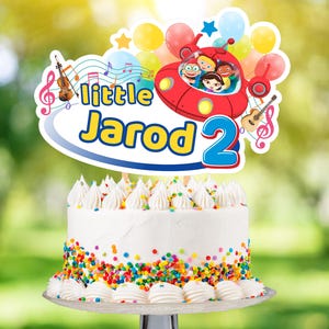 May include: A white cake with colourful sprinkles topped with a cake topper featuring the characters from the children's show "Little Einsteins". The topper says "little Jarod 2" and includes musical notes, a guitar, and a violin.