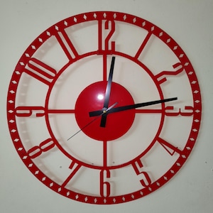 Puede incluir: Un reloj de pared rojo y circular con un diseño minimalista. El reloj presenta una esfera y un marco rojos con manecillas negras. Los números están recortados del marco. El reloj mide aproximadamente 46 cm de diámetro.