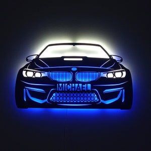 Könnte beinhalten: Eine schwarze Silhouette eines BMW-Autos mit blauen LED-Lichtern. Das Auto hat ein Nummernschild mit der Aufschrift "MICHAEL".