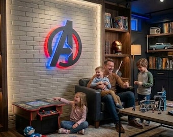 May include: A room featuring a large, illuminated Avengers logo mounted on a white brick wall. The space includes a small arcade game console, a plush Captain America toy, a leather armchair, a wooden coffee table, and built-in bookshelves.