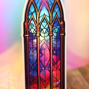 Könnte beinhalten: Ein Aufkleber mit einem Buntglasfenster-Design. Das Kunstwerk zeigt eine lebendige Farbpalette aus Blau-, Lila- und Rottönen mit einem himmlischen oder galaxieartigen Muster. Das Fenster ist mit goldfarbenen Linien und einem weißen Rand umrahmt.