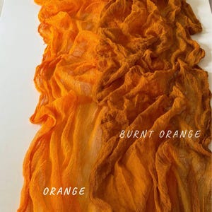Könnte beinhalten: Zwei Stücke orangefarbener Stoff, eines in einem helleren Orangeton und das andere in einem dunkleren, gebrannten Orange. Der Stoff ist strukturiert und hat ein zerknittertes Aussehen. Die Worte "ORANGE" und "GEBRANNTE ORANGE" sind auf dem Stoff geschrieben.