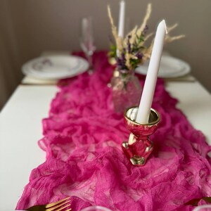 May include: A pink ruffled table runner with a gold metal candle holder and a white candle. The candle holder is shaped like a small animal.