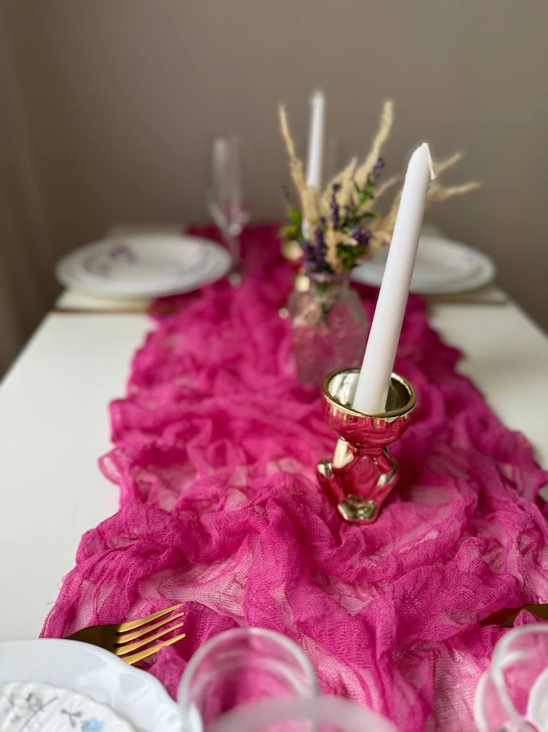 May include: A pink ruffled table runner with a gold metal candle holder and a white candle. The candle holder is shaped like a small animal.