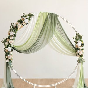 Peut inclure: Une arche circulaire en métal blanc décorée de draperies en tissu vert et blanc et de verdure avec des fleurs blanches et beiges.