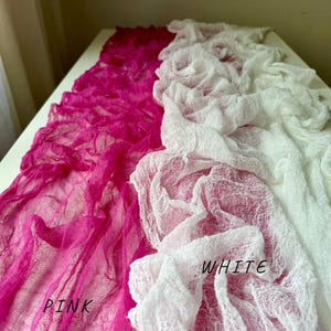 May include: Two pieces of sheer fabric, one pink and one white, are draped over a white surface. The fabric is textured and has a crinkled appearance. The words "PINK" and "WHITE" are written on the fabric.