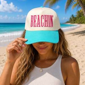 Peut inclure: Une casquette de baseball avec un panneau avant couleur crème portant le mot BEACHIN' brodé en lettres rose vif. La casquette possède une visière turquoise éclatante et un bouton turquoise assorti au sommet de la calotte.