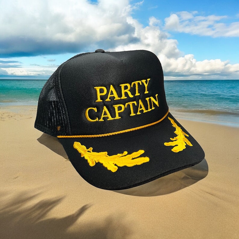 May include: Black trucker hat with a yellow mesh back and a gold embroidered rope trim. The hat has the words "PARTY CAPTAIN" embroidered in yellow on the front.