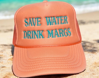 May include: A peach-colored foam trucker hat featuring a structured front panel with the embroidered teal text "SAVE WATER DRINK MARGS" and a matching orange cord trim across the base of the crown, paired with a curved brim and mesh back panels.