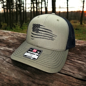 May include: A green and black baseball cap with a distressed American flag design. The cap is made by Richardson 112.