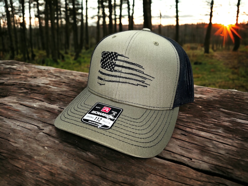 May include: A green and black baseball cap with a distressed American flag design. The cap is made by Richardson 112.