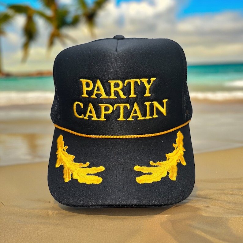 May include: Black mesh trucker hat with gold embroidery that reads "PARTY CAPTAIN". The hat has two gold embroidered leaf designs on the sides.
