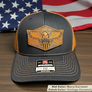 Navy and caramel trucker hat with a vintage caramel patch. The patch features an eagle, the text "250 YEARS 1776 AMERICA 2026", and the Richardson logo. The hat is adjustable.