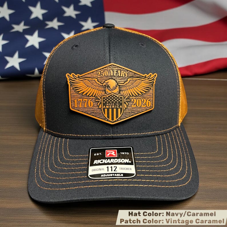 Navy and caramel trucker hat with a vintage caramel patch. The patch features an eagle, the text "250 YEARS 1776 AMERICA 2026", and the Richardson logo. The hat is adjustable.