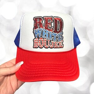 May include: A red, white, and blue trucker hat with the words "RED WHITE BOUEEE" in a patriotic design. The hat has a red peak, a white front panel, and a blue mesh back.